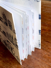 Load image into Gallery viewer, Open cookbook with pages showing illustrations on a wooden surface