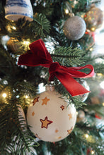 Load image into Gallery viewer, Hand painted yellow stars on a white background design Christmas ornament with red ribbon on a tree