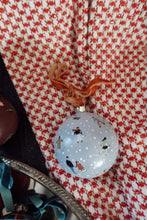 Load image into Gallery viewer, Hand painted Christmas ornament with tiny skaters on a snowy blue background. The ornament is displayed on red check fabric