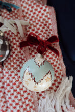 Load image into Gallery viewer, Hand painted Christmas ornament with a white background, blue chevron stripe and yellow stars. Displayed with a red ribbon on a checkered fabric background