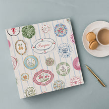 Load image into Gallery viewer, Recipe book with decorative cover featuring watercolor illustrations of china plate on a blue background with a cup of coffee and cookies.